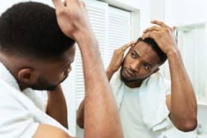 Young african man checking for thinning hair in mirror at bathroom