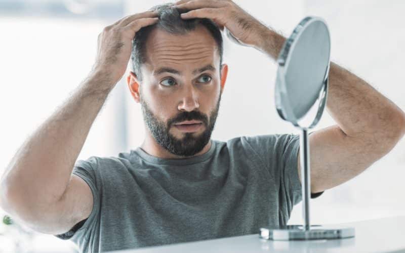 bearded mid adult man with alopecia looking at mirror, hair loss concept