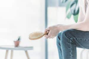 cropped shot of young woman holding hairbrush while sitting indoors, hair loss concept