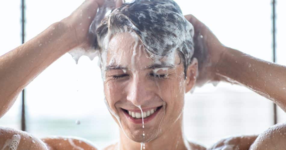 Handsome young male model washing hair with shampoo