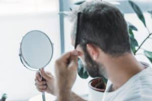 middle aged man combing hair and looking at mirror, hair loss concept